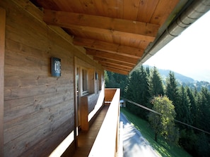 A wooden cabin with a balcony overlooking a forested valley.