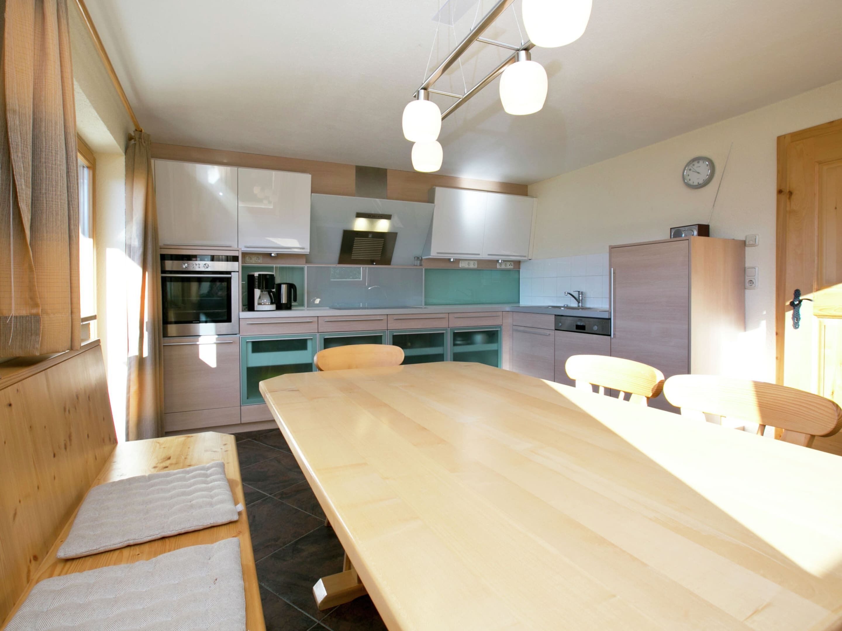 Een moderne keuken met een houten eettafel, inbouwapparatuur en een klok aan de muur.