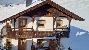 Ett hus i chaletstil med en träbalkong, en matplats med bord och stolar och ett snötäckt landskap.
