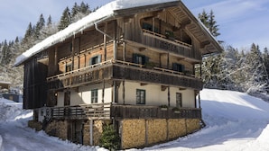 A multi-story wooden chalet with balconies, surrounded by snow-covered trees. - Farmhouse in Hopfgarten Near Ski Bus (Hopfgarten im Brixental)