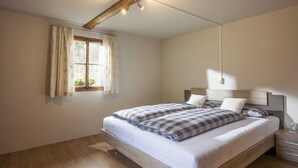 A bedroom with a wooden bed, a window with curtains, and a ceiling light fixture. - Farmhouse in Hopfgarten Near Ski Bus (Hopfgarten im Brixental)