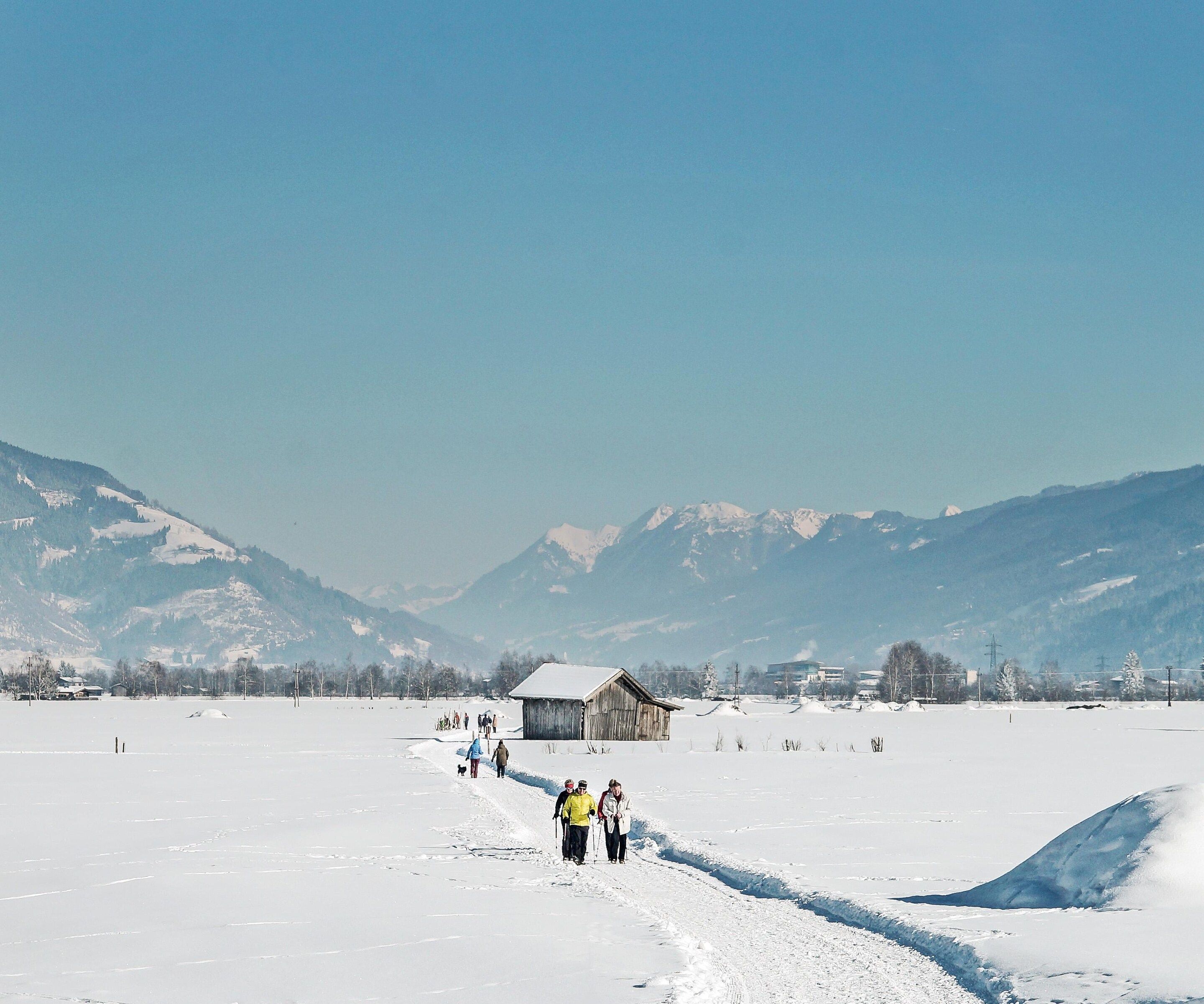 A snowy landscape with a clear sky, a wooden building, and mountains in the background.