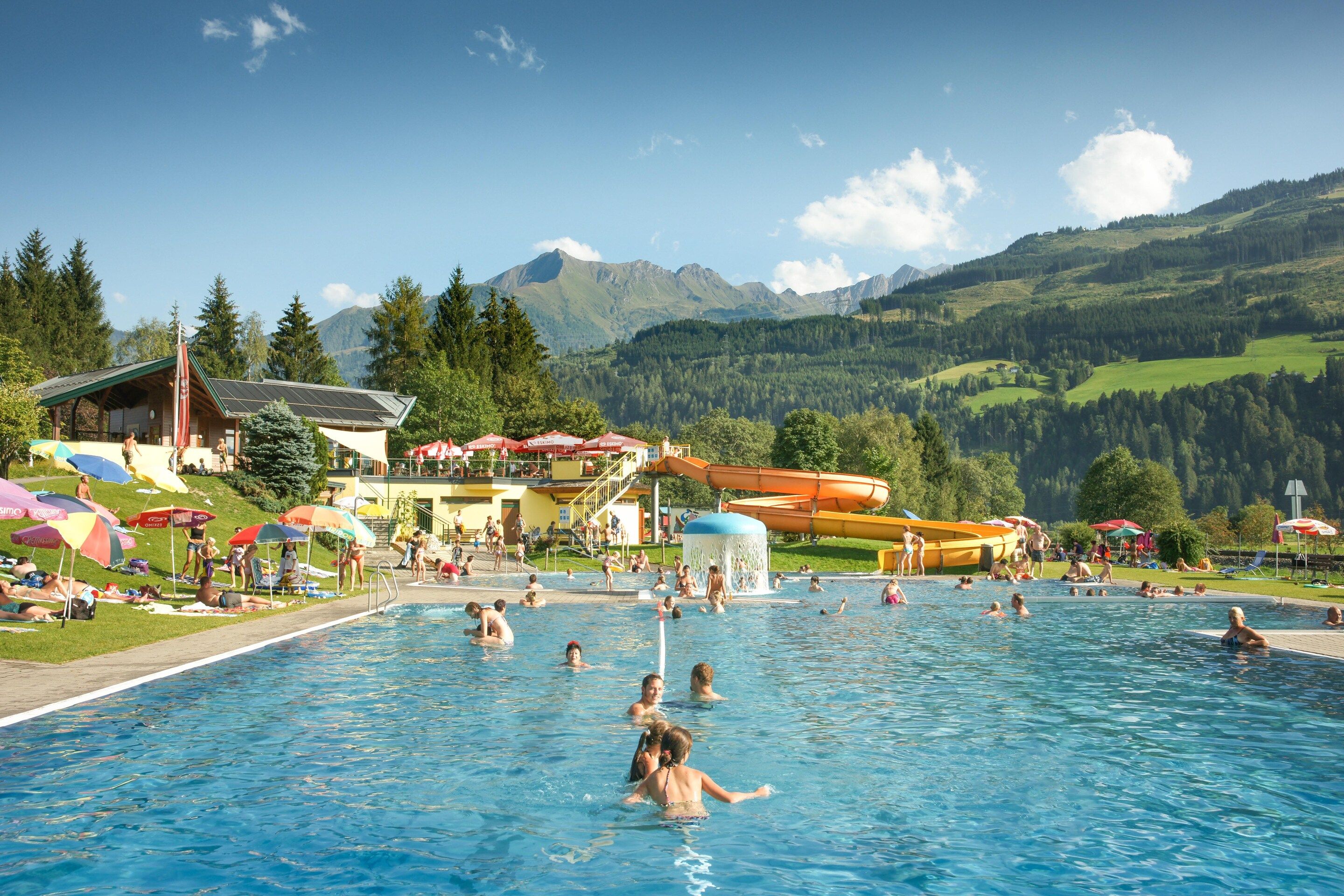 A swimming pool with people, a water slide, and a mountain backdrop.