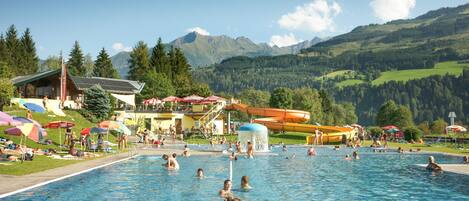 A swimming pool with people, a water slide, and a mountain backdrop.