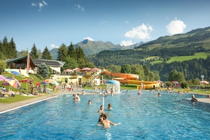 A swimming pool with people, a water slide, and a mountain backdrop. - Chalet in Piesendorf Near Ski Slopes (Piesendorf)
