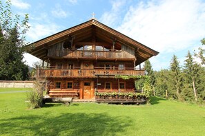 A wooden chalet with a balcony, a front porch, and a cross on the roof.