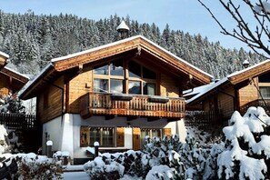 En træchalet med balkon, omgivet af sneklædte træer.