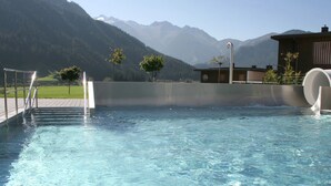 A clear pool with a metal ladder, surrounded by a wooden deck and a mountain backdrop. - Premium Chalet With Sauna on a Sunny Slope (Neukirchen am Grossvenediger)