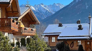 A wooden chalet with a balcony, surrounded by snow-covered mountains and a clear sky. - Premium Chalet With Sauna on a Sunny Slope (Neukirchen am Grossvenediger)