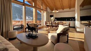 A spacious living area with a high ceiling, large windows offering a mountain view, a dining area, and a kitchen. - Premium Chalet With Sauna on a Sunny Slope (Neukirchen am Grossvenediger)