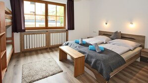 A bedroom with a wooden bed, a bench, a window with curtains, and a view of a wooden deck outside. - Apartment at the City Center in Brandberg (Brandberg)