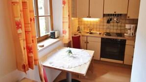Een kleine keuken met een raam, een tafel met een kantone kleedje, en voorzieningen zoals een broodrooster en koffiezetapparaat.