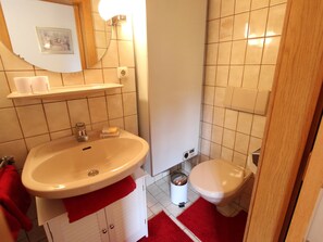 Un baño con un lavamanos blanco, un inodoro, una alfombra de baño roja y un espejo.