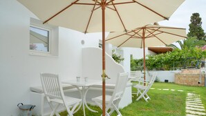 A patio with white furniture, a large umbrella, and a stone wall. - Moschoula studios (Milos)