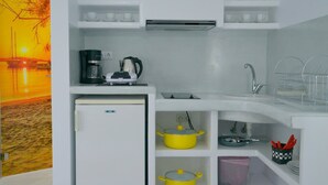 A compact kitchenette with a refrigerator, coffee maker, kettle, and yellow pots. - Moschoula studios (Milos)