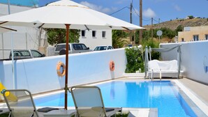 A pool area with lounge chairs and umbrellas, a lifebuoy, and a view of the surrounding buildings and landscape. - Moschoula studios (Milos)