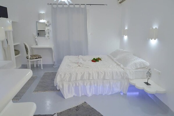 A white-themed bedroom with a bed, bedside table, and a chair. - Moschoula studios (Milos)