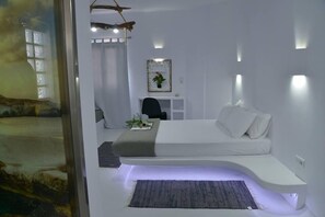 A modern bedroom with a curved bed, a desk, and a chair. - Moschoula studios (Milos)