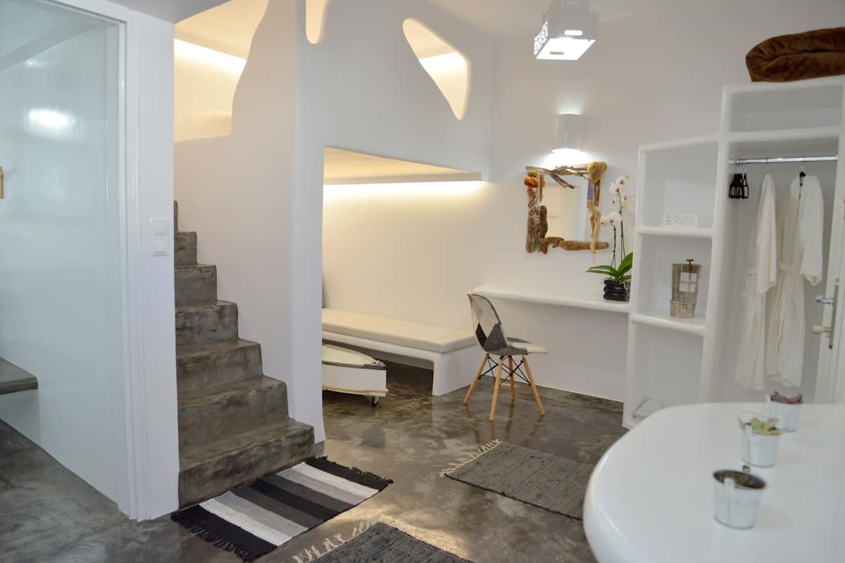 Une salle de bain moderne avec un lavabo blanc, un miroir et un espace douche. Un escalier mène à une autre pièce.