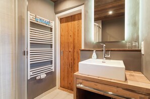 A modern bathroom with a wooden door, a white towel rack, a white sink, and a mirror above the sink. - Chalet in Ellmau Near Ski Slopes (Ellmau)