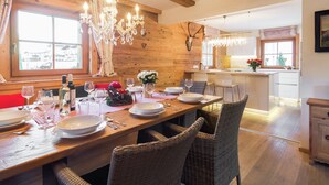 A dining area with a wooden table set for four, surrounded by wicker chairs. A chandelier hangs above, and a deer skull decorates the wall. - Chalet in Ellmau Near Ski Slopes (Ellmau)
