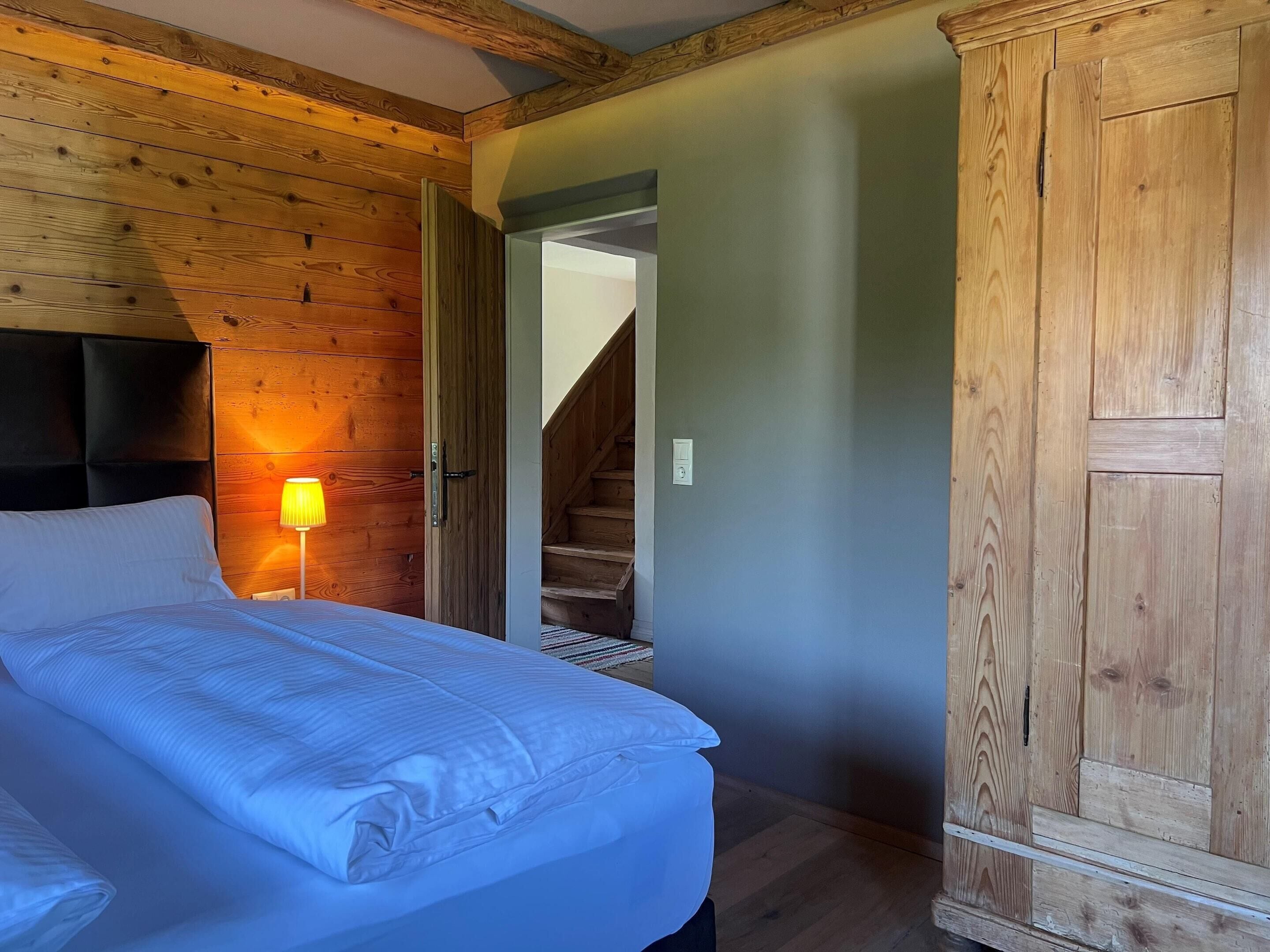 Une chambre à coucher avec une tête de lit en bois, un lit recouvert de draps blancs, une lampe de chevet et une armoire.