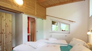 Une chambre avec un plafond en bois, une fenêtre donnant sur un paysage verdoyant et un lit recouvert de draps blancs.