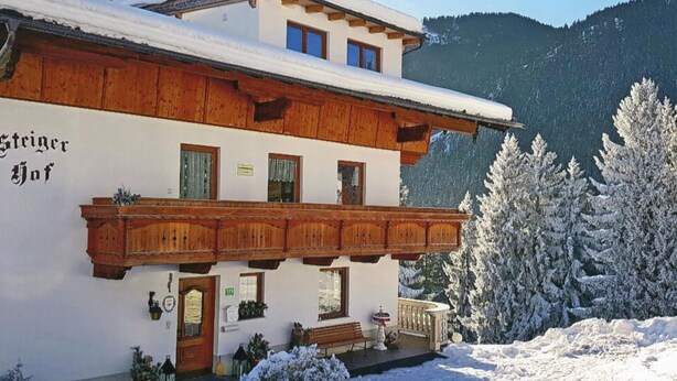 Un bâtiment de style alpin traditionnel, doté d’un balcon en bois, d’un toit enneigé et surplombant un paysage montagneux.