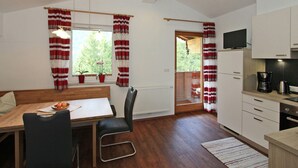 Une cuisine moderne avec des meubles blancs, un coin repas doté d’une table et de chaises en bois, et une vue sur la verdure à l’extérieur.