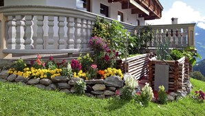 Un chalet traditionnel doté d’une balustrade en pierre, de parterres fleuris aux couleurs vives et d’une structure en bois.