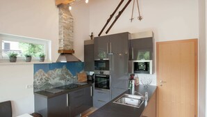 A modern kitchen with a stone backsplash, stainless steel appliances, and a wooden dining table. - Stunning Holiday Home With Balcony, Ski Storage, Parking (Maria Alm am Steinernen Meer)