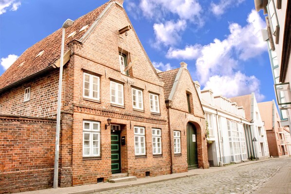 Ein traditionelles Backsteingebäude mit einem steilen Satteldach, großen Fenstern und einer grünen Tür.