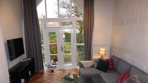 A living room with a grey sofa, a black coffee table, a TV on a black stand, and a large window with curtains. - Altstadtzauber Lüneburg (Lueneburg)