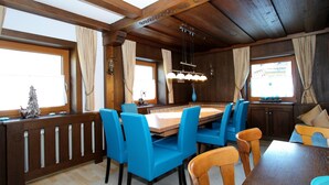 A dining area with a wooden table and blue chairs, large windows with curtains, and a chandelier. - Spacious Chalet near Ski Area in Itter (Itter)