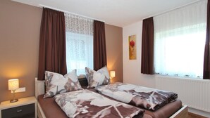 A double bed with a floral bedspread, two bedside tables with lamps, a window with curtains, and a radiator. - Spacious Chalet near Ski Area in Itter (Itter)