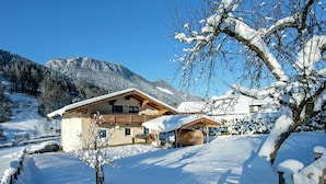 A snow-covered mountain house with a wooden balcony, a wooden barrel, and a clear blue sky. - Spacious Chalet near Ski Area in Itter (Itter)