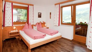 A cozy bedroom with a wooden bed, two bedside tables, a window with curtains, and a view of the outdoors.