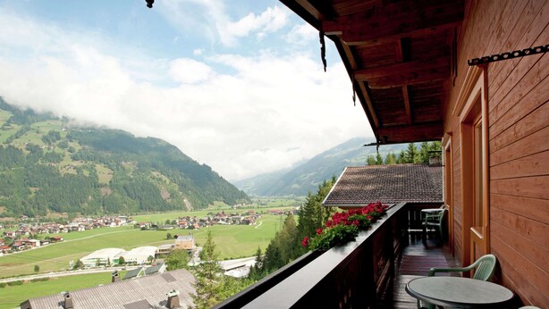 A wooden balcony with a view of a valley and mountains.