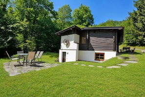 Une cabane en rondins avec un patio en pierre, une table à manger avec des chaises et une petite fenêtre.