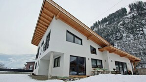 A modern two-story house with a sloped roof, large windows, and a wooden exterior.