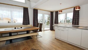 A modern kitchen with wooden flooring, white cabinets, a built-in bench, and a large window with curtains.