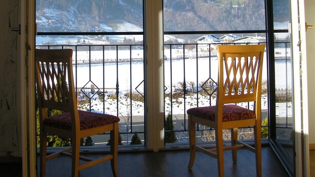 A room with two wooden chairs facing a large sliding glass door leading to a snowy outdoor area with a view of a hilly landscape.
