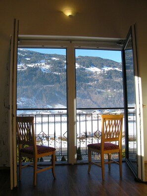 Une pièce avec deux chaises en bois, placées face à une grande porte-fenêtre coulissante qui donne sur un espace extérieur enneigé, offrant une vue sur un paysage vallonné.