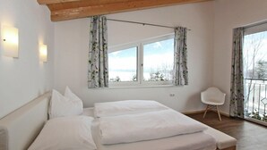 A bedroom with a wooden ceiling, a bed with white linens, a window with floral curtains, and a view of a snowy landscape.