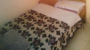 A small bed with a floral bedspread, a wooden headboard, and a blue curtain. - Jupiter House (Kitengela)