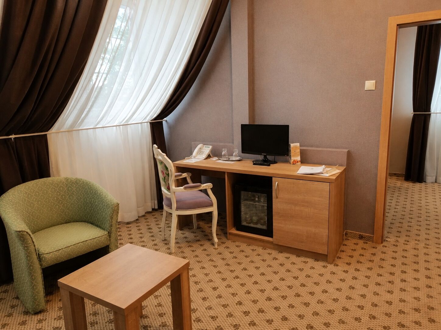 A hotel room with a desk, chair, and a small table.