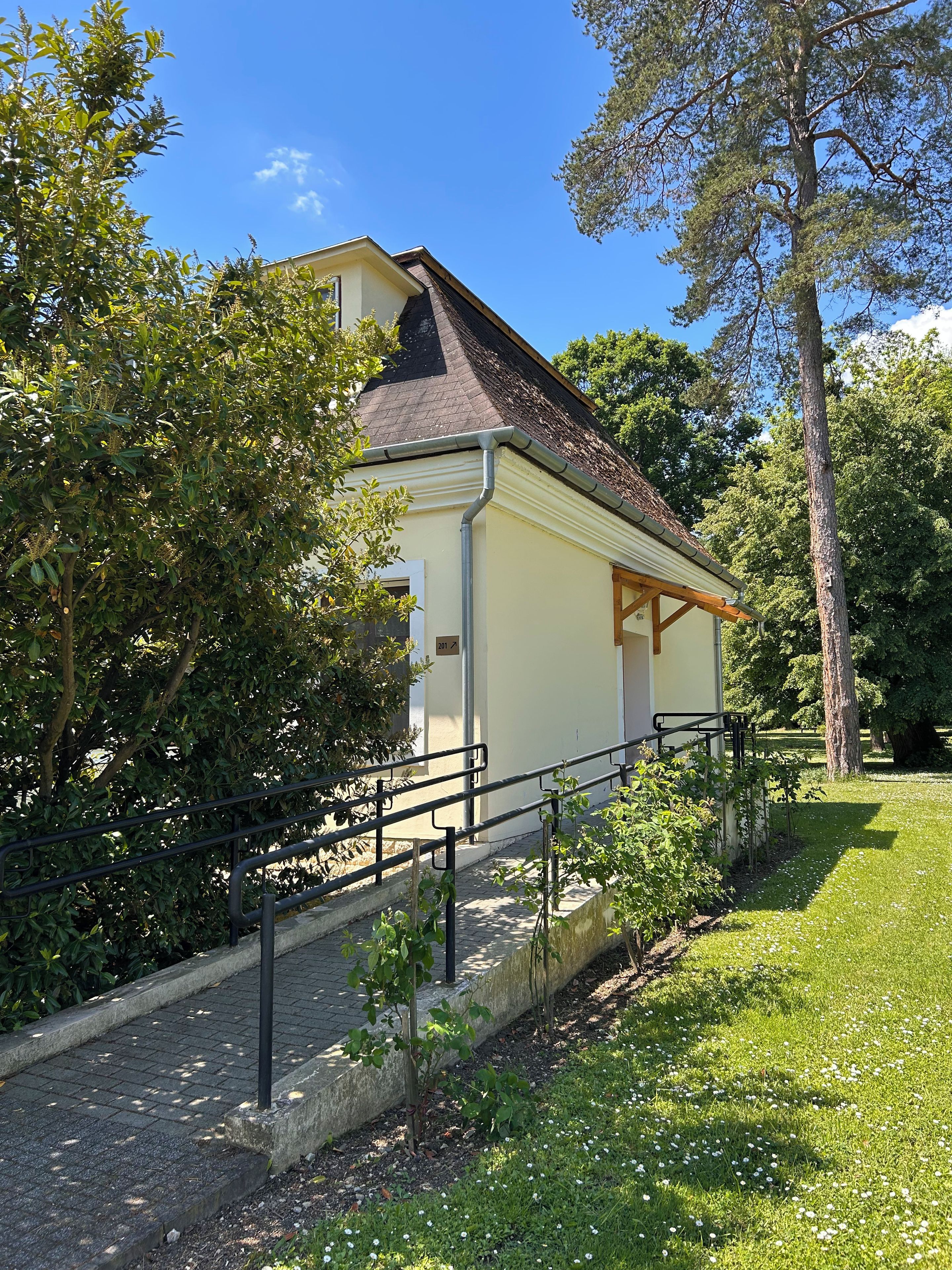 Ein Gebäude mit einem geneigten Dach, einer kleinen Veranda und einem gepflasterten Weg, der dorthin führt.