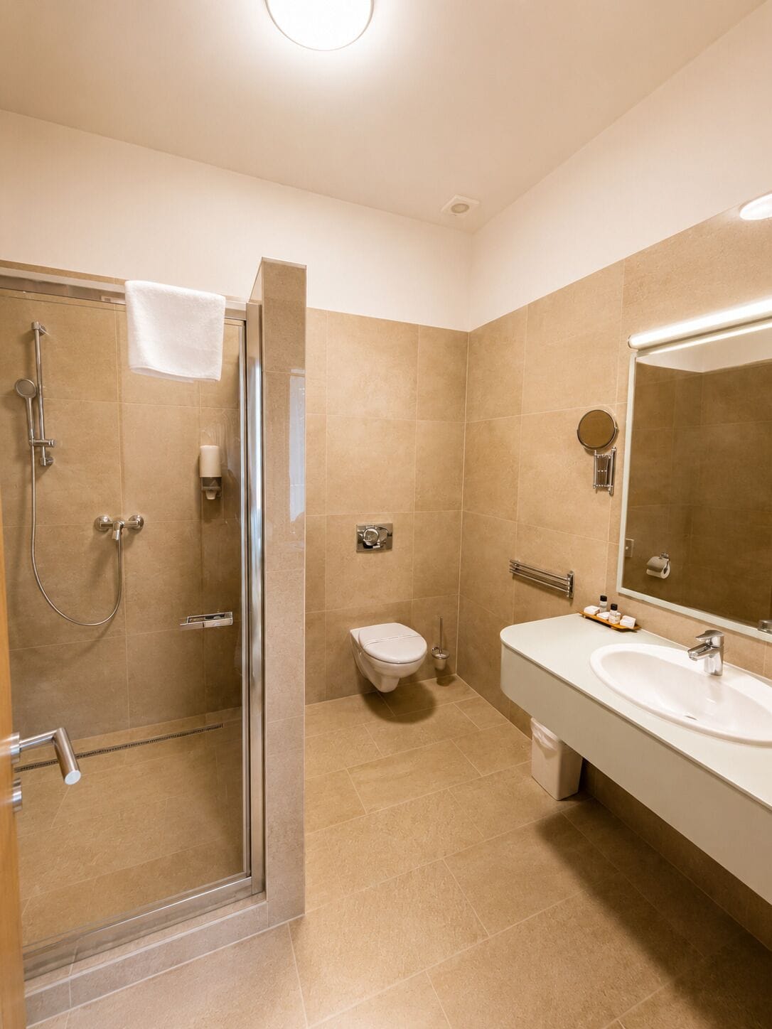 Moderni kylpyhuone, jossa on lasiseinällä varustettu suihku, wc ja peilillä varustettu pesuallas.