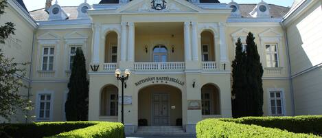 A stately building with a symmetrical facade, a central entrance with a balcony, and a sign indicating it is a hotel.
