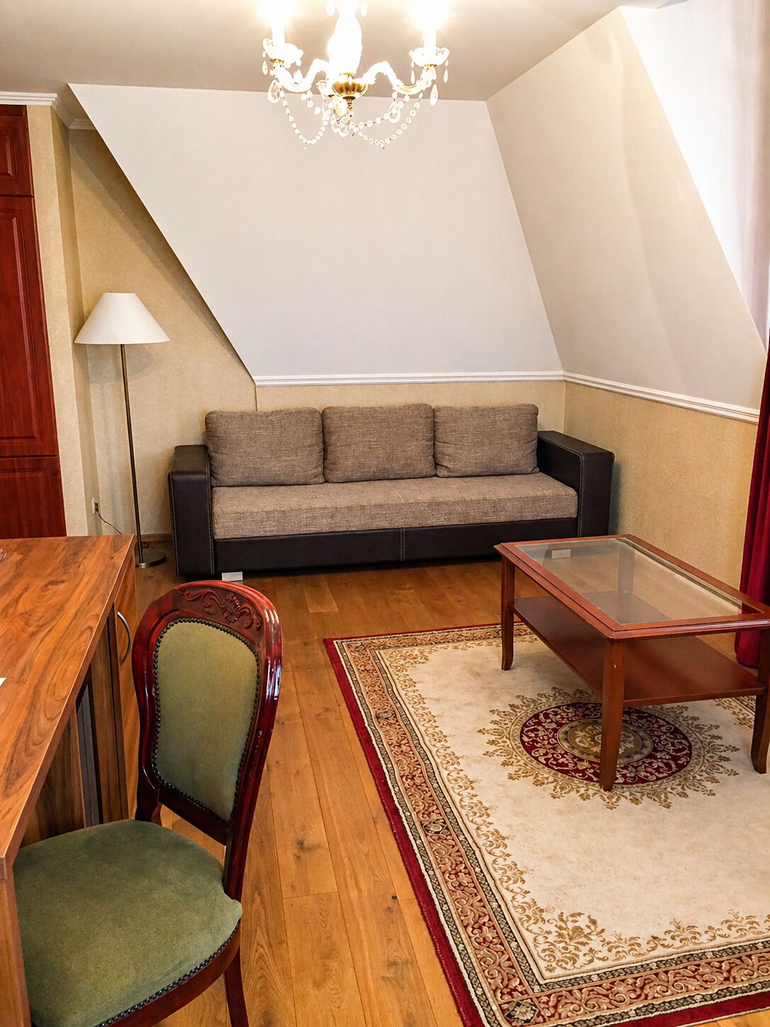 A loft-style room with a sofa, a glass-top table, a wooden dining table, a chair, and a patterned rug.
